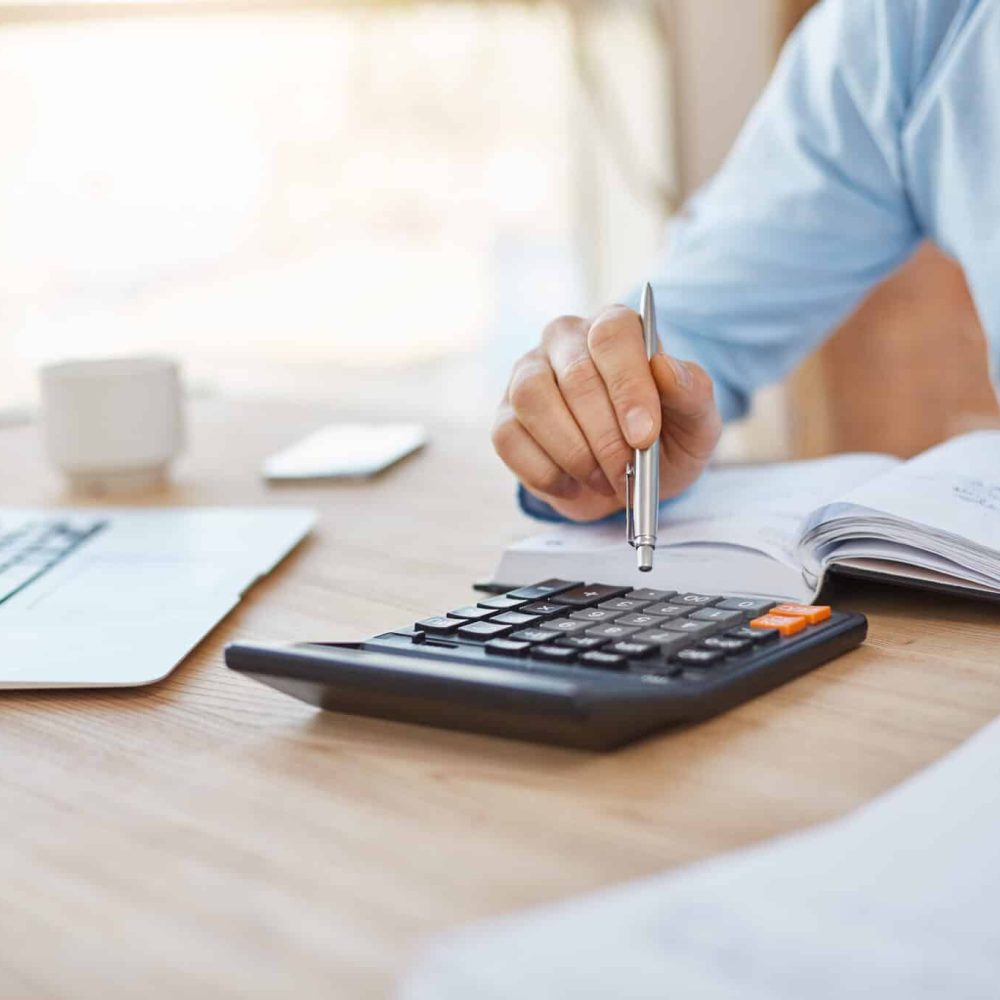 Close up detail of professional serious accountant sitting in light office, checking company finance profits on calculator, writing down results in notebook. Business concept.